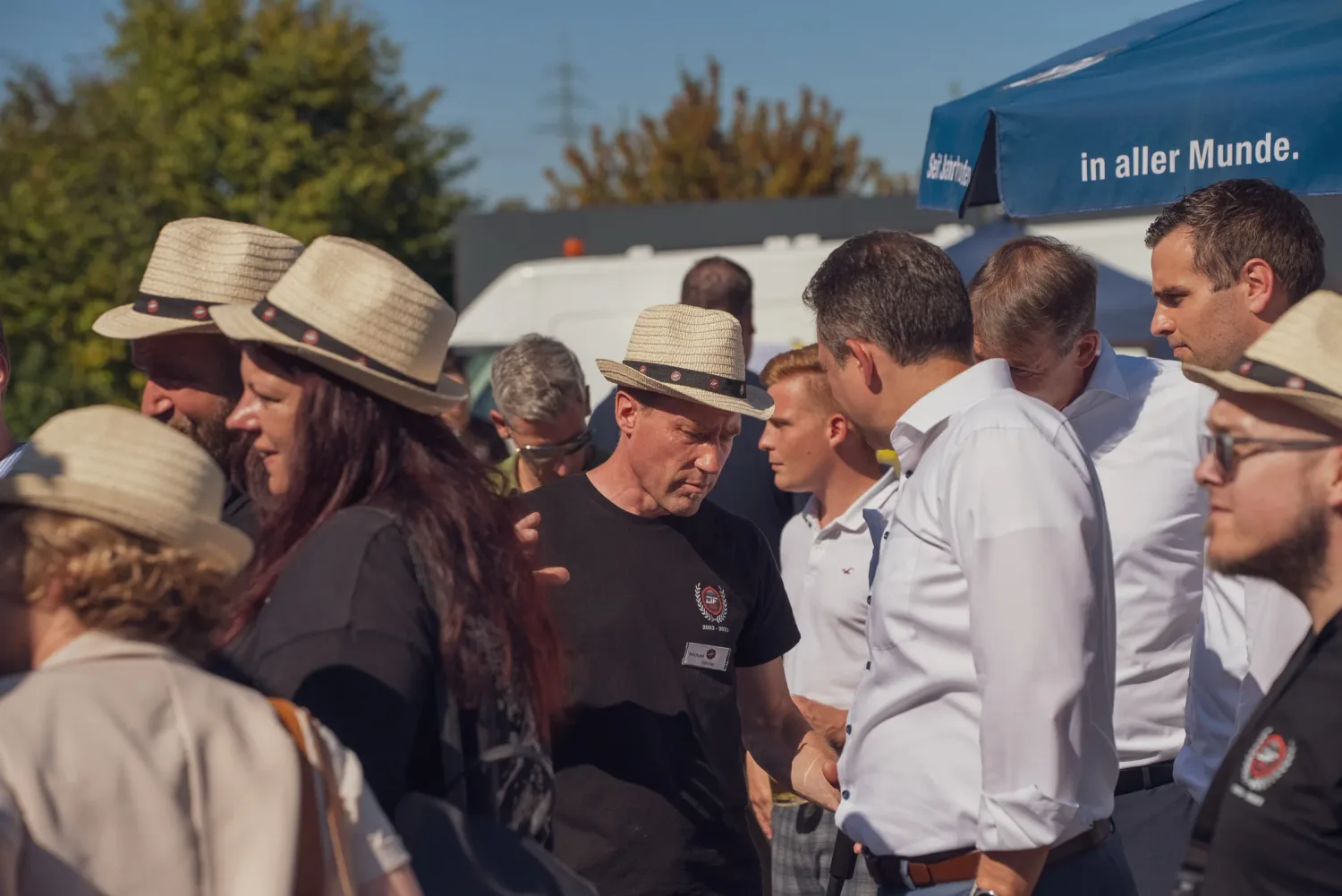 Eventfotograf beim Sommerfest: Gästegruppe mit Jubiläums-Strohhüten im Gespräch