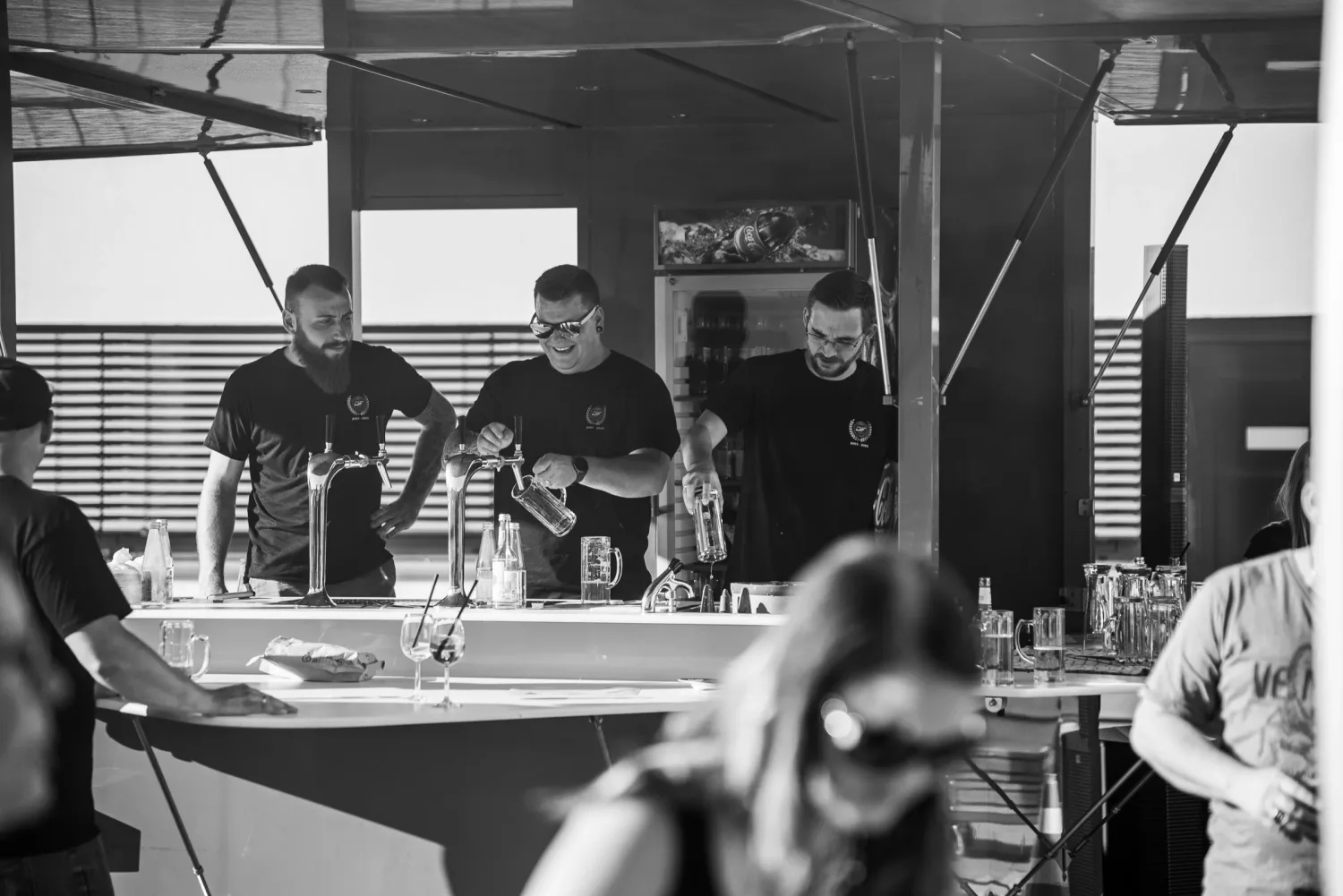 Eventfotograf beim Firmenjubiläum: drei Helfer zapfen Bier in der Ausschank, dokumentarisch in Schwarz-Weiß