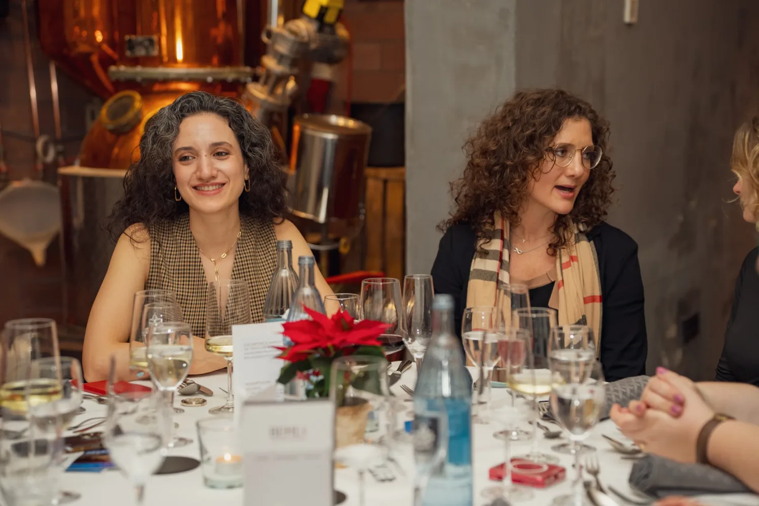 Eventfotograf bei der Weihnachtsfeier: zwei Gäste im Gespräch am festlich gedeckten Tisch vor den Kupferkesseln der Brennerei