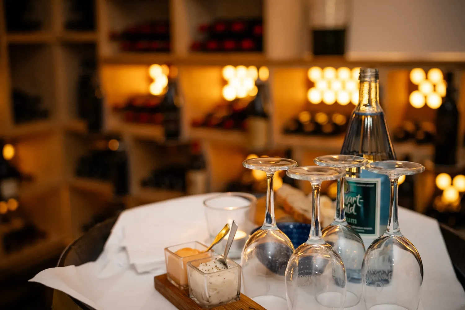 Eventfotografie Firmenfeier: gedeckter Tisch mit Amuse-Bouche und Weingläsern vor dem Weinregal im Brennhaus Behl