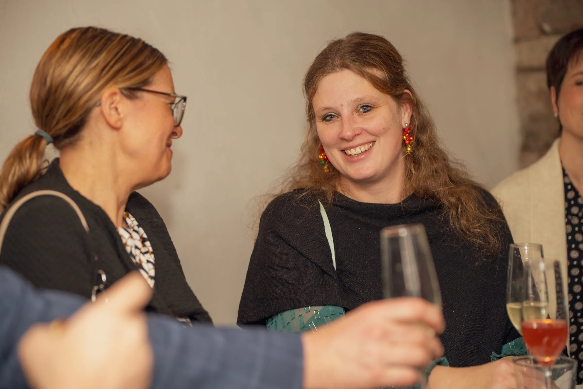 Eventfotograf Weihnachtsfeier: Gästin mit weihnachtlichen Ohrringen strahlt beim Sektempfang