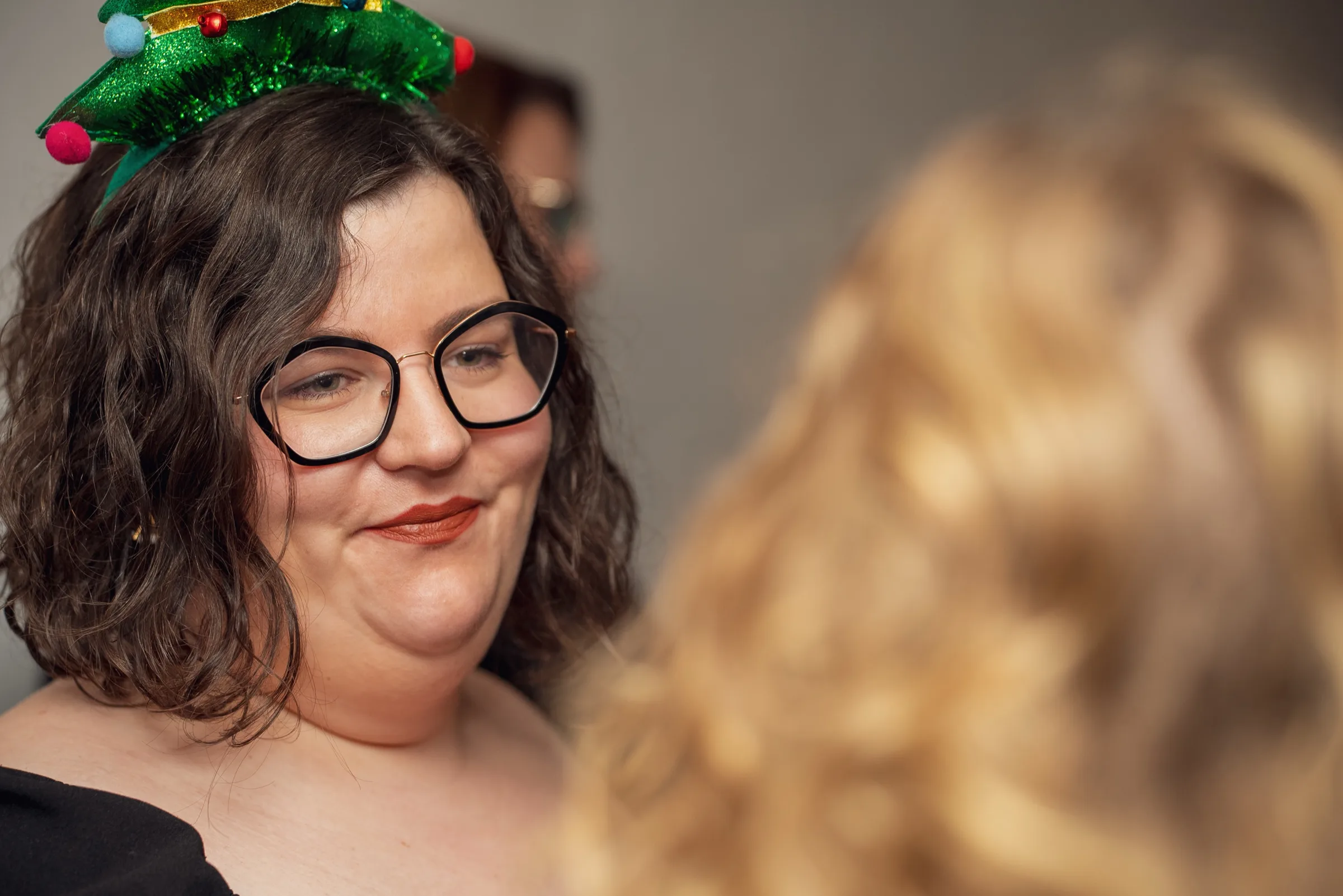 Eventfotografie bei der Weihnachtsfeier: Gästin mit Weihnachtsbaum-Fascinator lächelt schelmisch