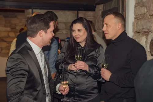 Eventfotograf Weihnachtsfeier Aschaffenburg: drei Gäste beim Sektempfang vor Natursteinwand