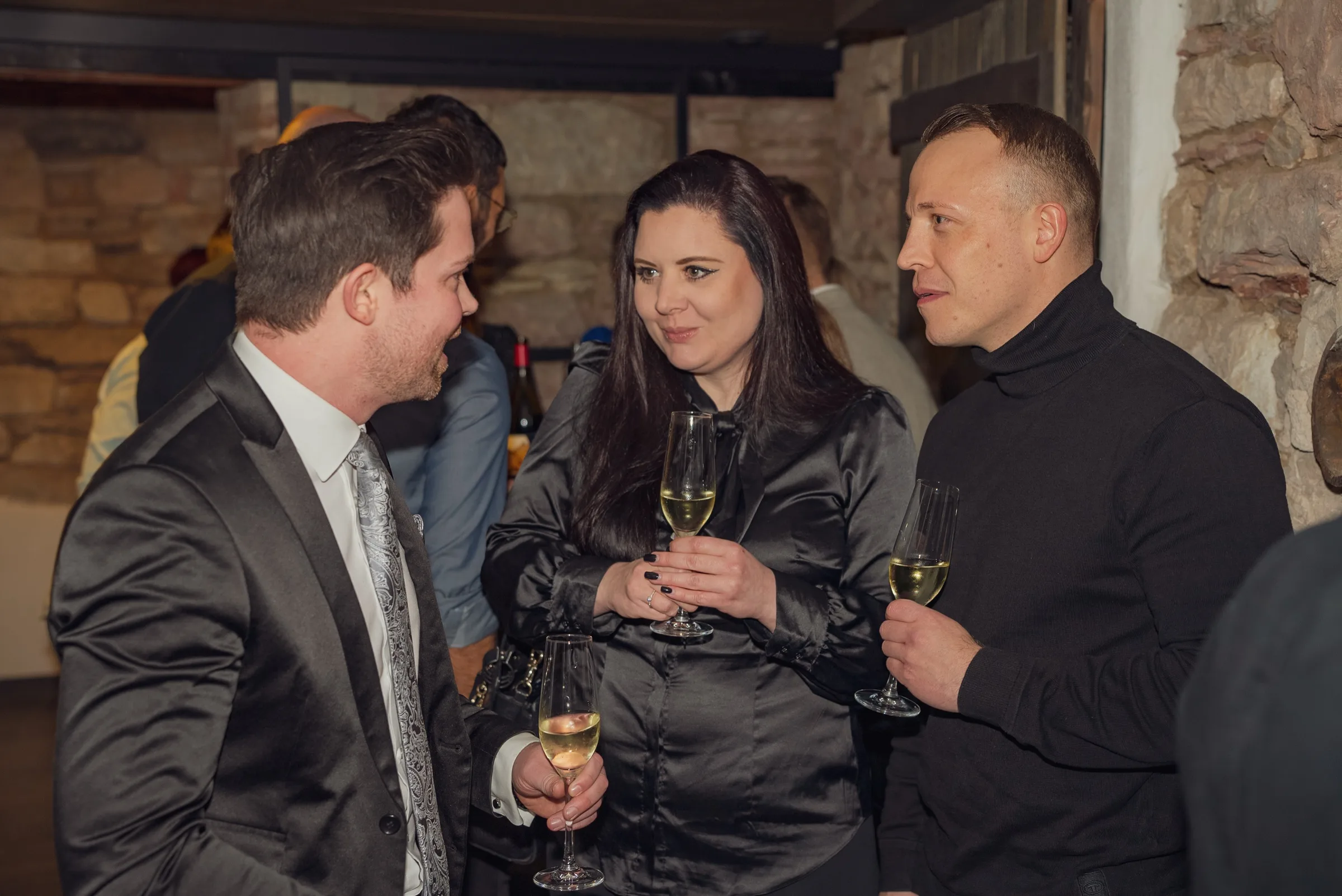 Eventfotograf Weihnachtsfeier Aschaffenburg: drei Gäste beim Sektempfang vor Natursteinwand