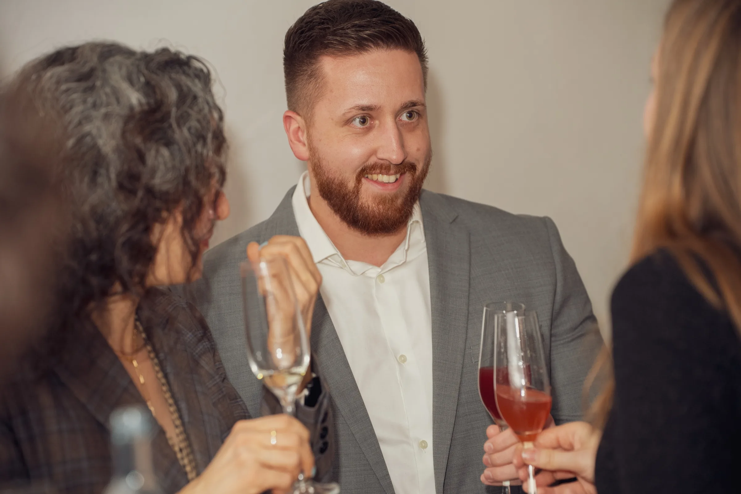 Eventfotografie bei der Weihnachtsfeier: Gast lächelt im Sektempfang zwischen zwei Gästen