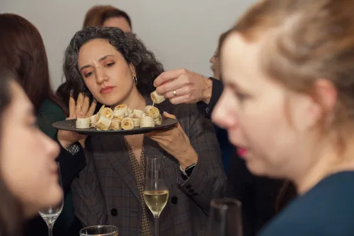 Eventfotografie Firmenfeier: Gastgeberin reicht eine Platte mit Wrap-Spießen beim Empfang