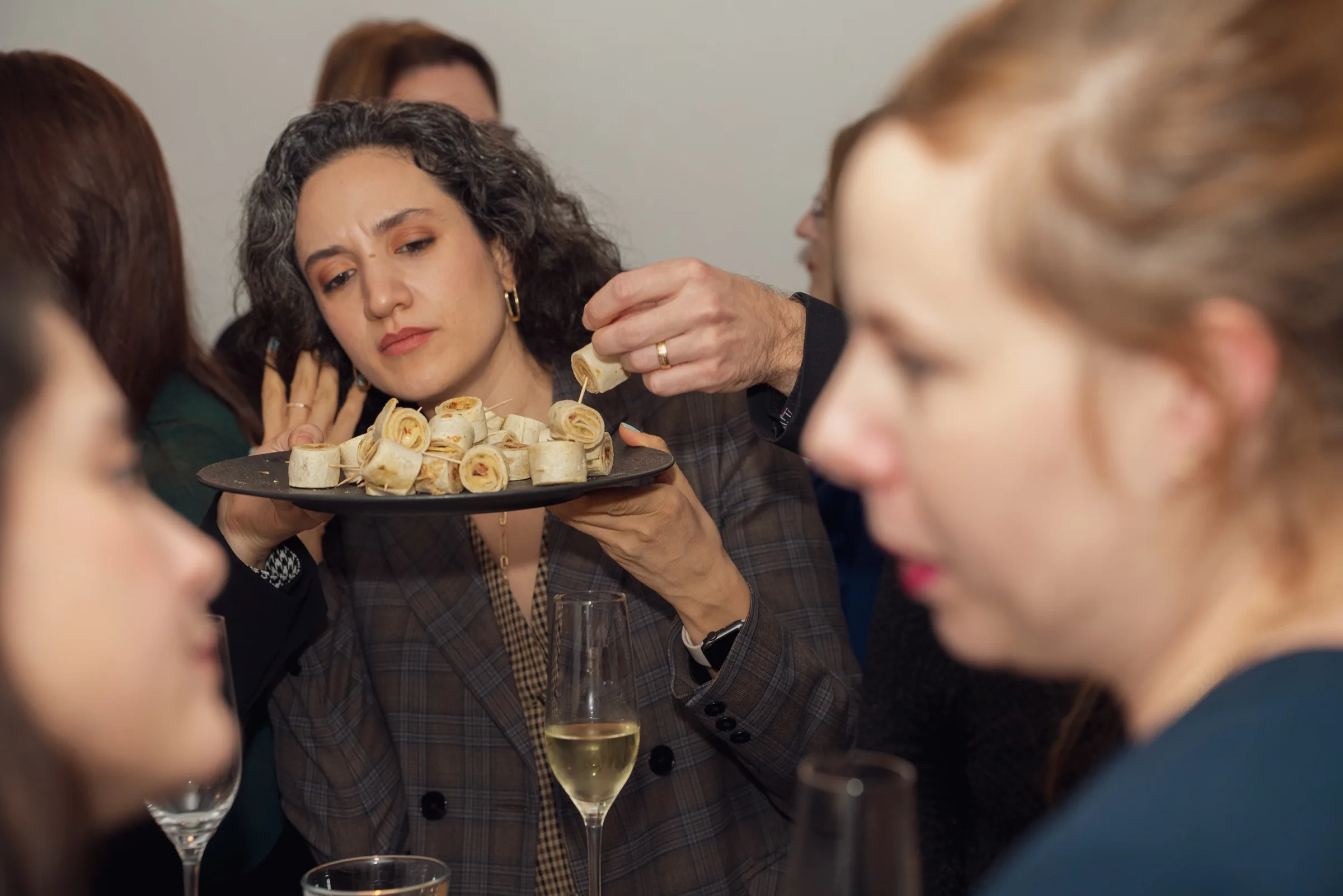 Eventfotografie Firmenfeier: Gastgeberin reicht eine Platte mit Wrap-Spießen beim Empfang