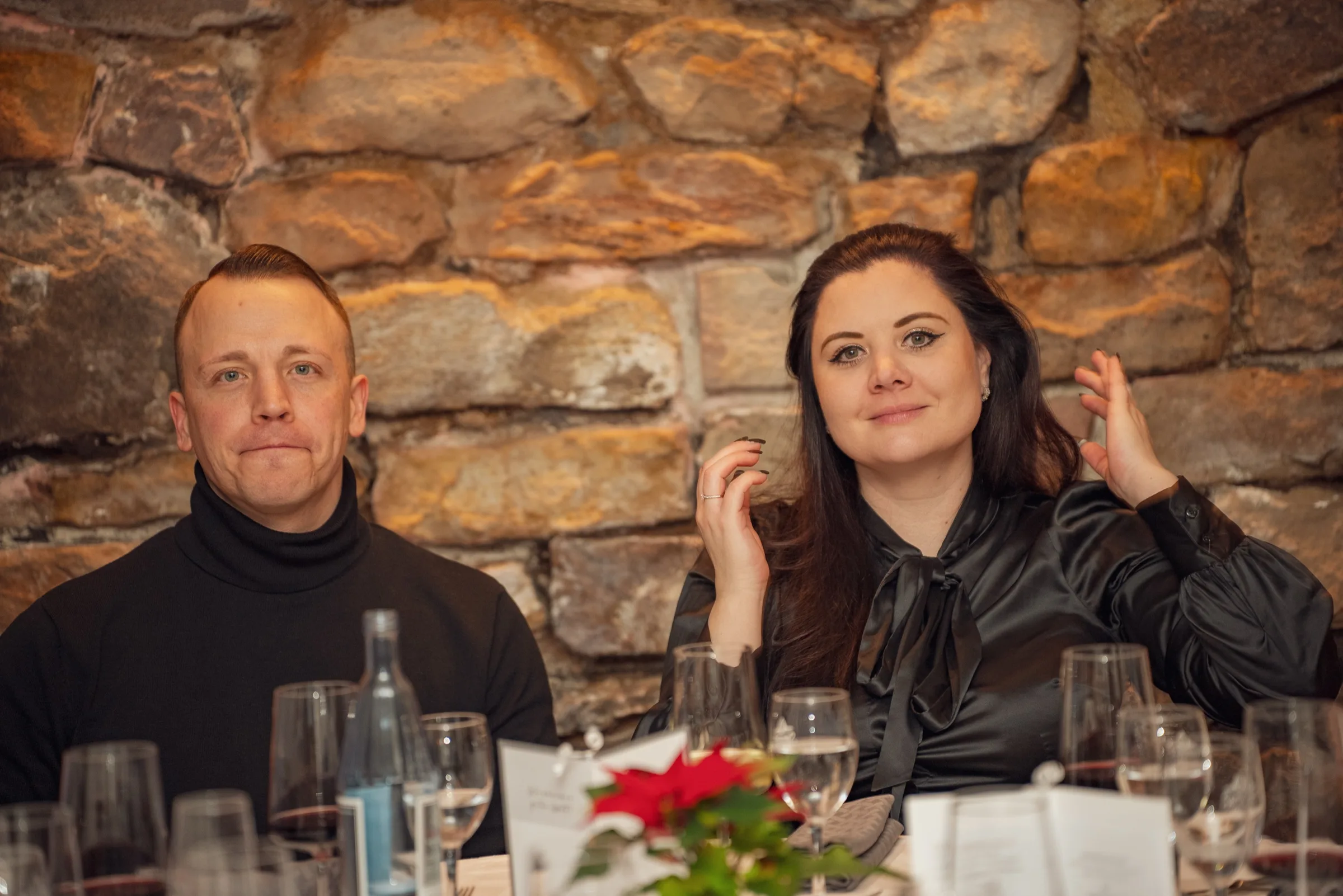 Eventfotograf Firmenfeier: zwei Gäste sitzen nebeneinander vor der Natursteinwand