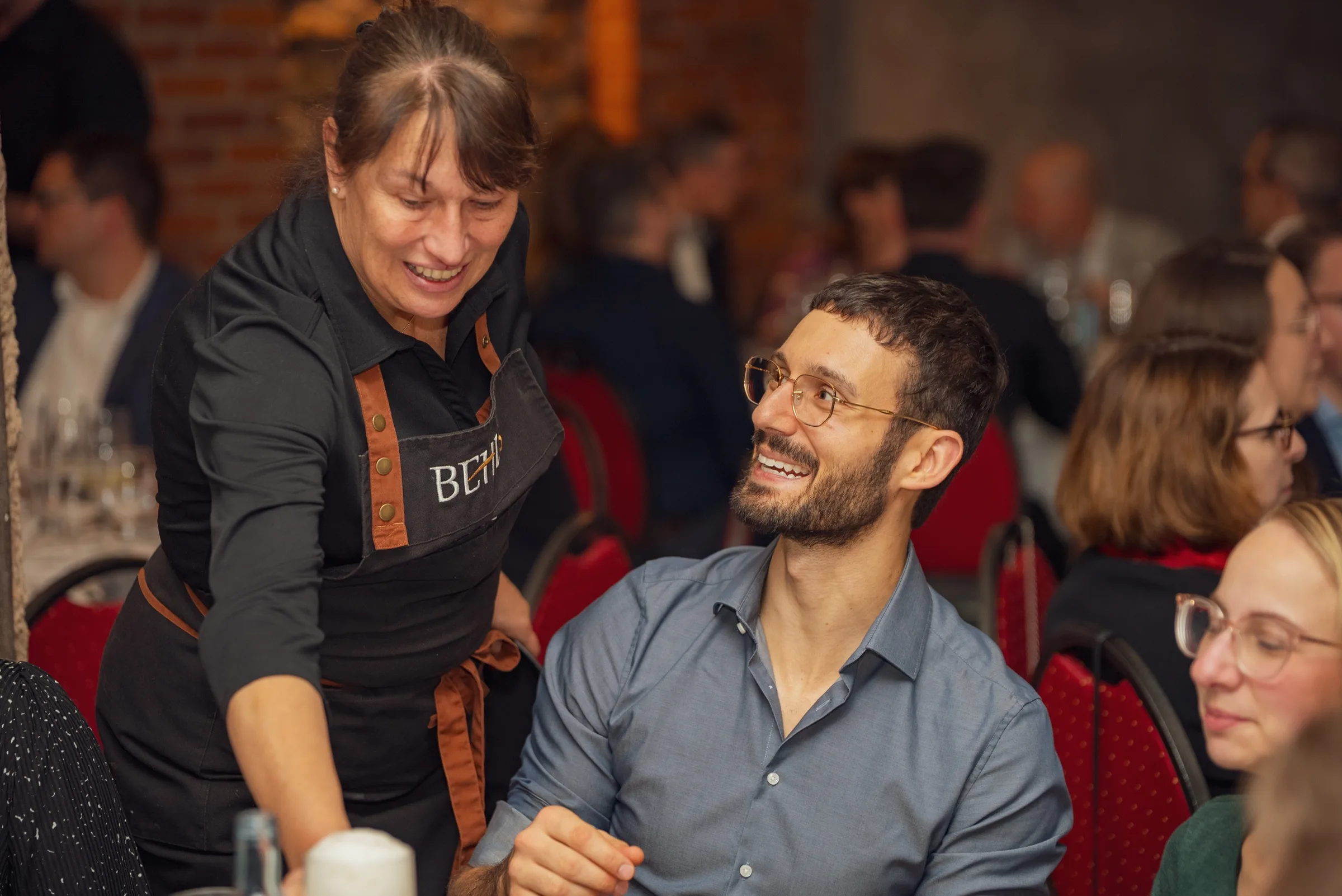 Eventfotograf Weihnachtsfeier: Bedienung mit Brennhaus-Behl-Schürze im Gespräch mit einem Gast