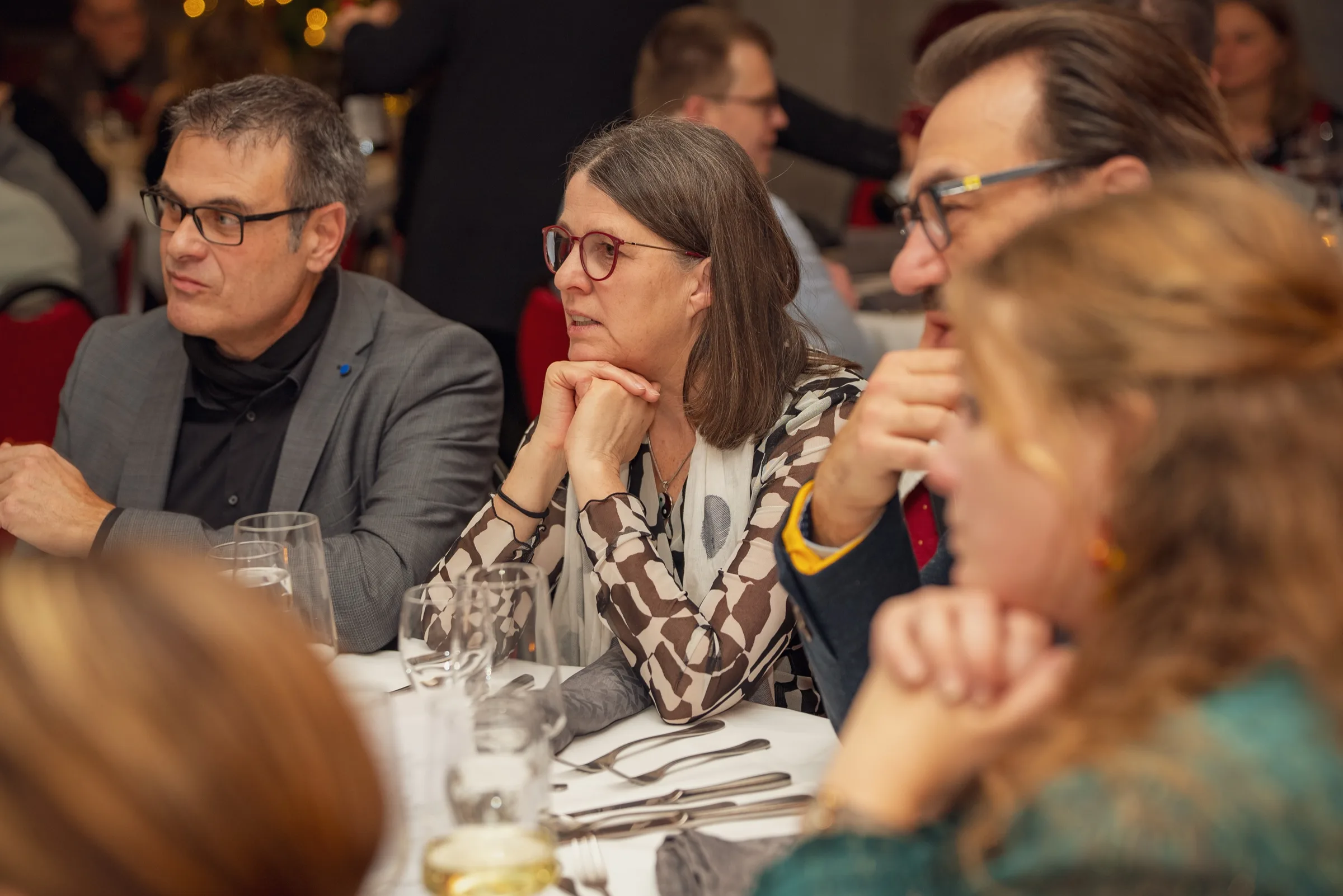 Eventfotografie bei der Weihnachtsfeier: Tischrunde hört aufmerksam einer Rede zu