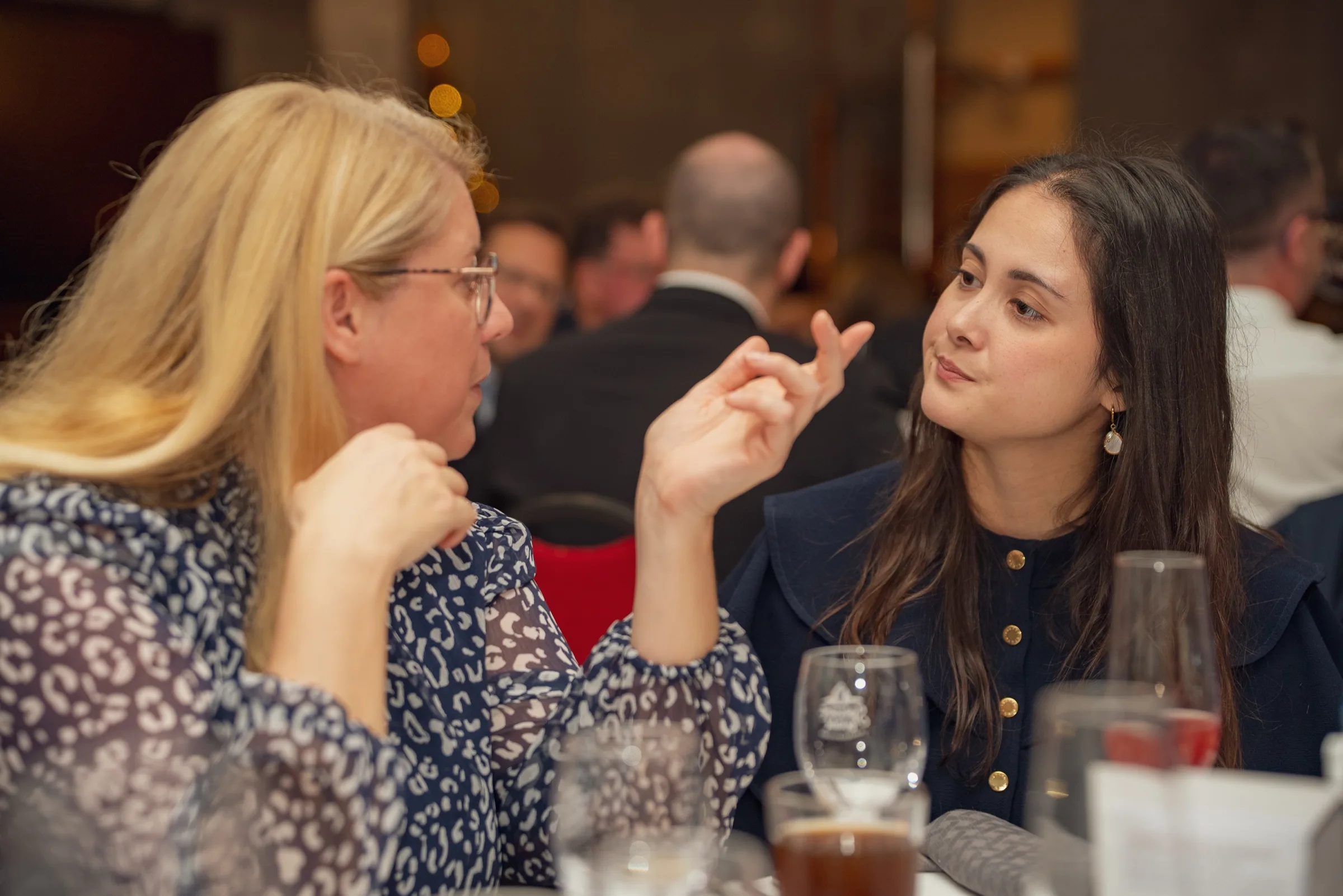 Eventfotografie Firmenfeier: zwei Gäste im lebhaften Gespräch mit Handgeste am Tisch