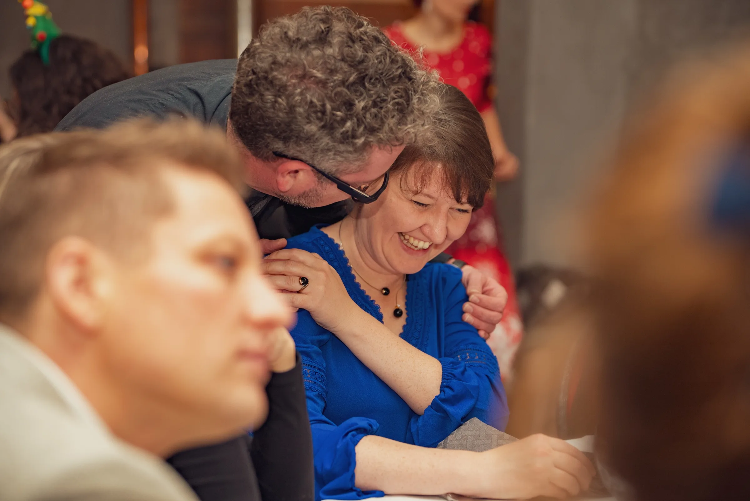 Eventfotograf Weihnachtsfeier: herzliche Umarmung zwischen zwei Gästen am Tisch