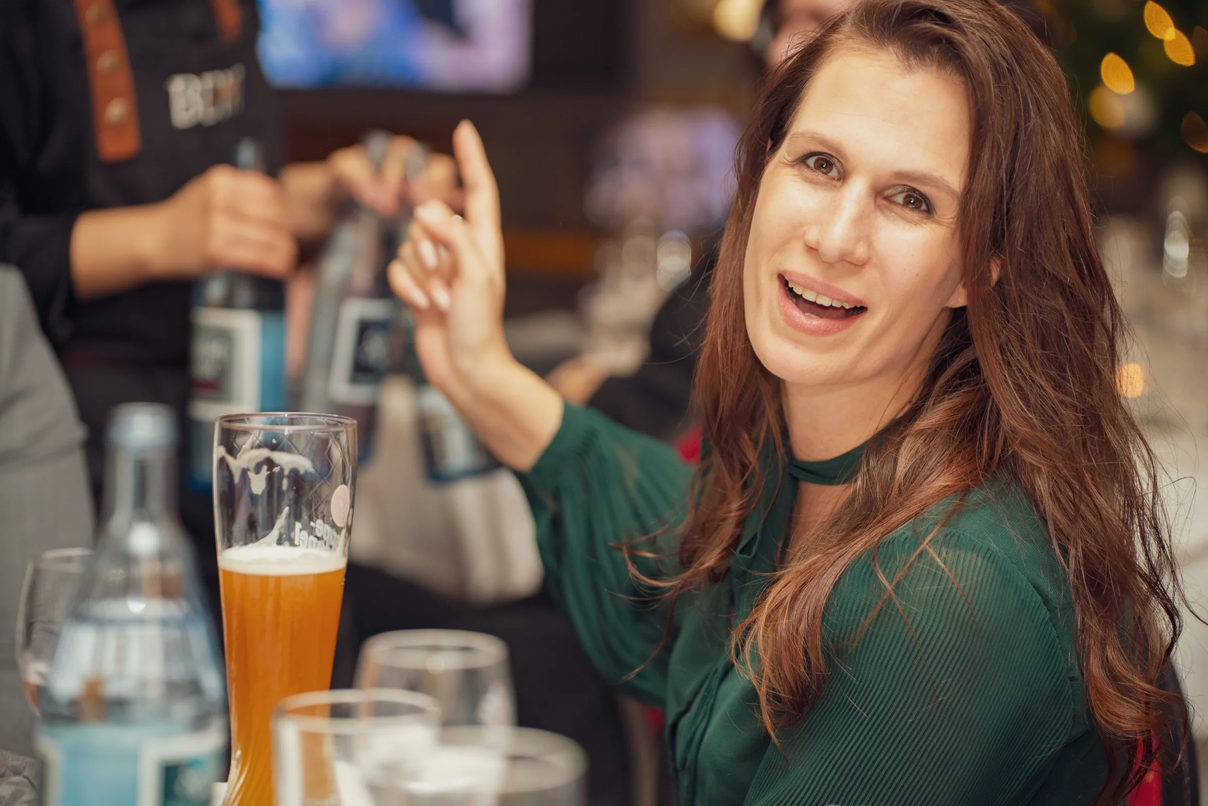 Eventfotograf Weihnachtsfeier: Gästin mit Weizenbier gestikuliert lebhaft im Gespräch