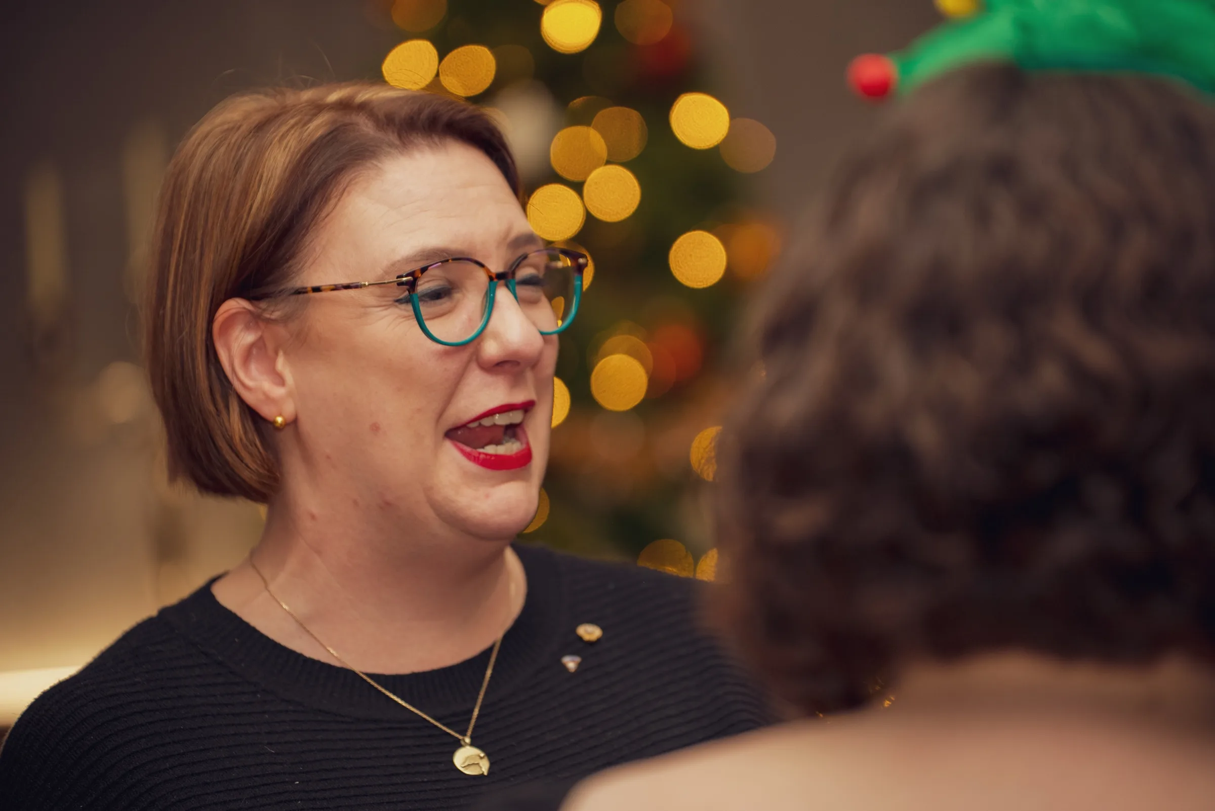 Eventfotograf bei der Weihnachtsfeier: Gästin lacht im Gespräch vor dem geschmückten Weihnachtsbaum